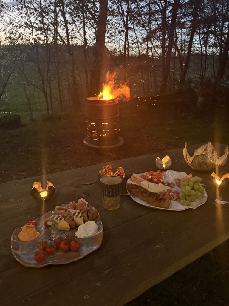 Deko Gartenparty Sommer Gemütlich dekorierter Gartentisch für eine Sommerparty mit Keramik, Windlichtern und Snacks am Feuer